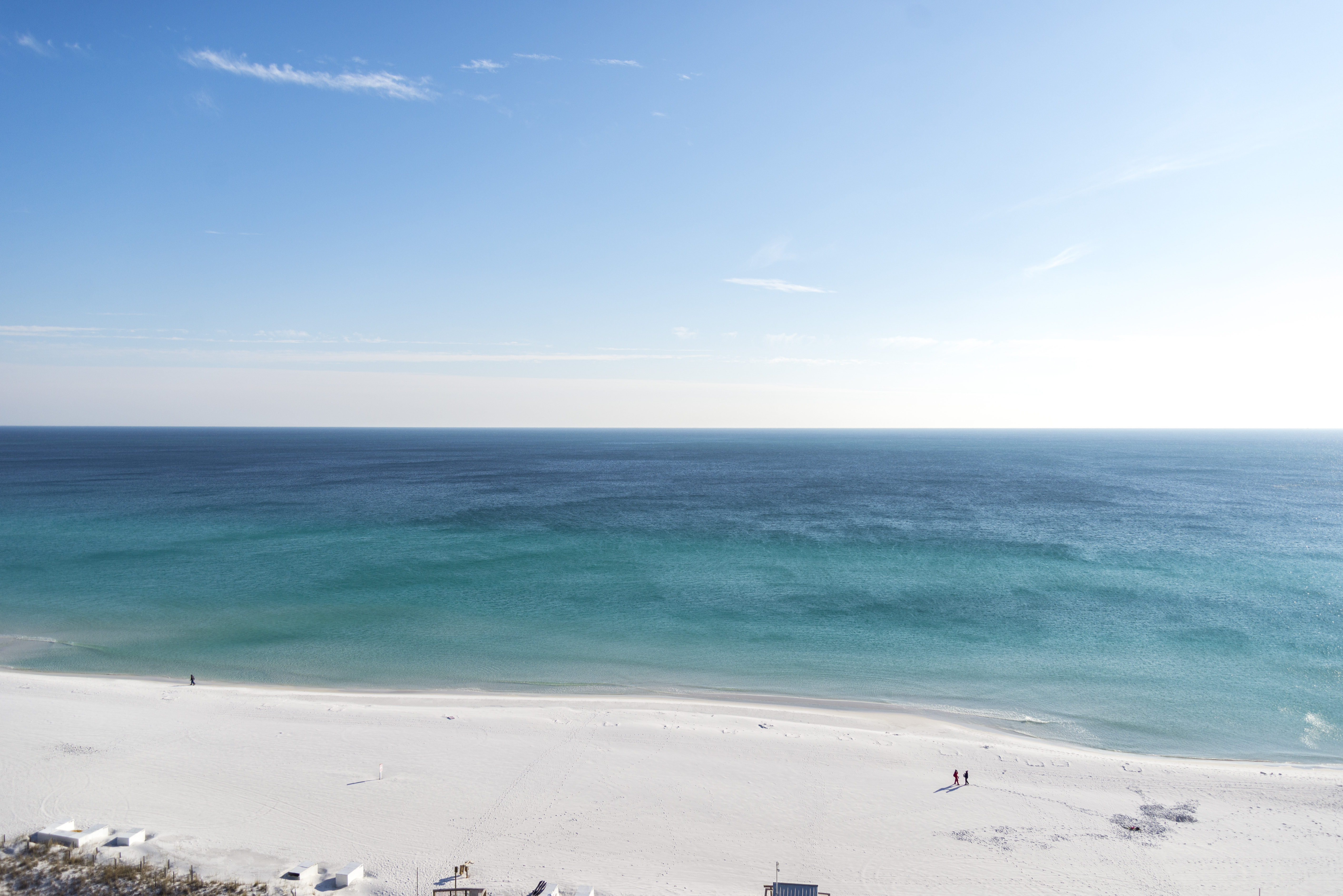 a view of the beach with 3 people taking a stroll on the beach from their vacation rentals home.