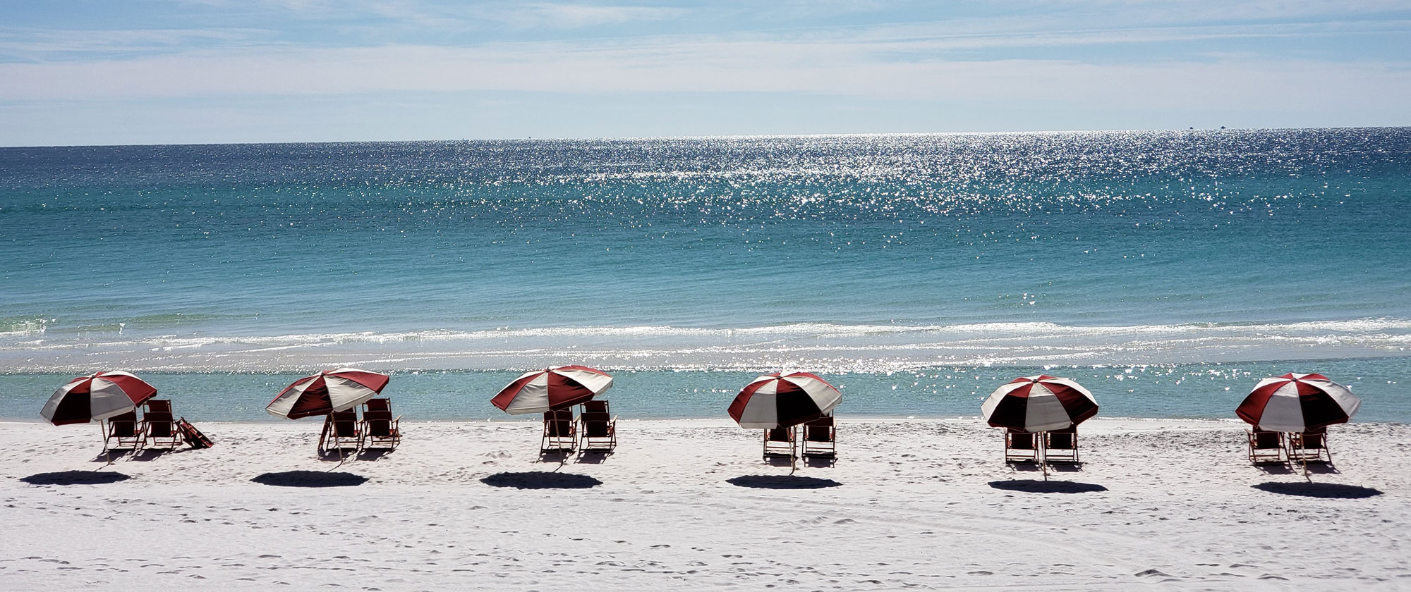 Beach and ocean with 12 sun-bathing chairs and 6 red-white umbrellas